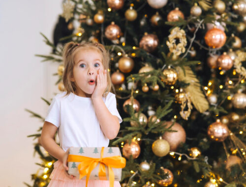 charming-little-surprised-girl-holds-gift-background-christmas-trees