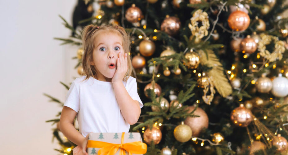 charming-little-surprised-girl-holds-gift-background-christmas-trees