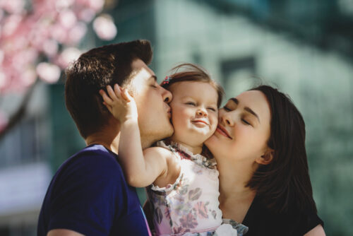 happy-young-parents-with-little-daughter-stand-blooming-pink-tree-outside